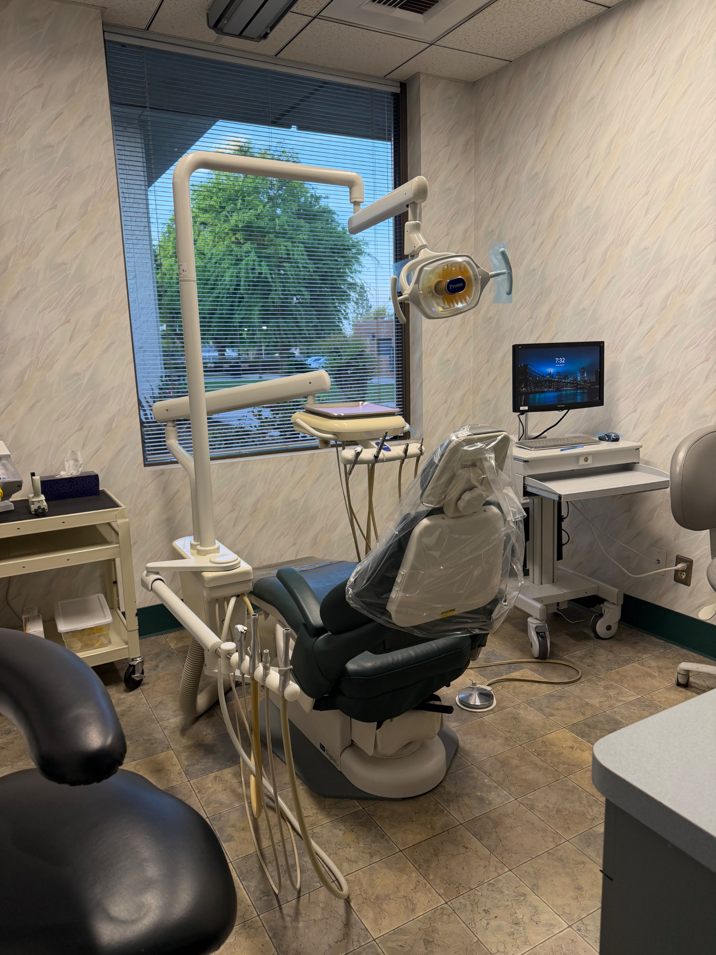 Bright dental treatment room with chair, overhead light and monitor